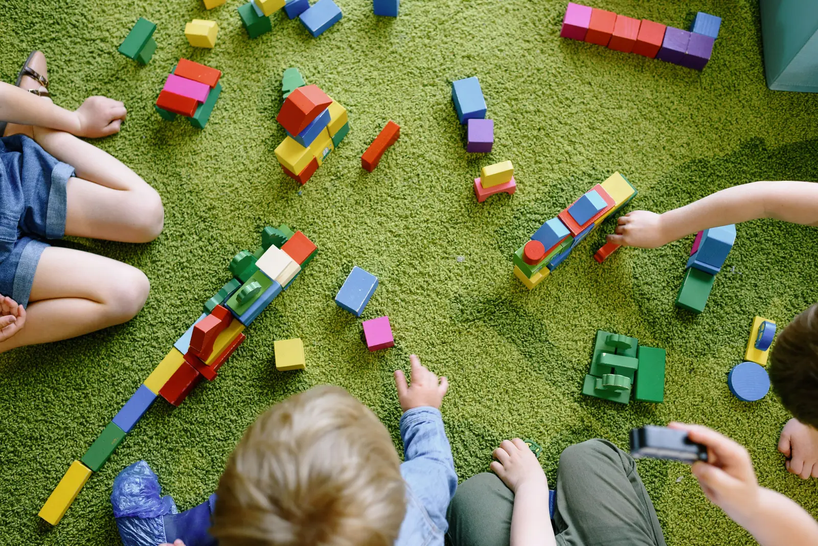 Des enfants construisent avec des blocs de bois colorés sur un tapis vert