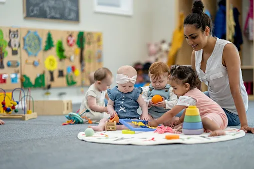 Une éducatrice joue avec des bébés sur un tapis
